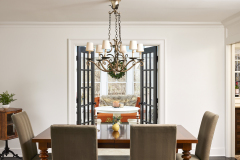 Dining room remodeling project. Dining room refresh. First floor remodel. A large wooden table sits in the centre surrounded by four chairs. A chandelier hangs down  in the center of the photo. A sun room is just visible through a double set of french doors 