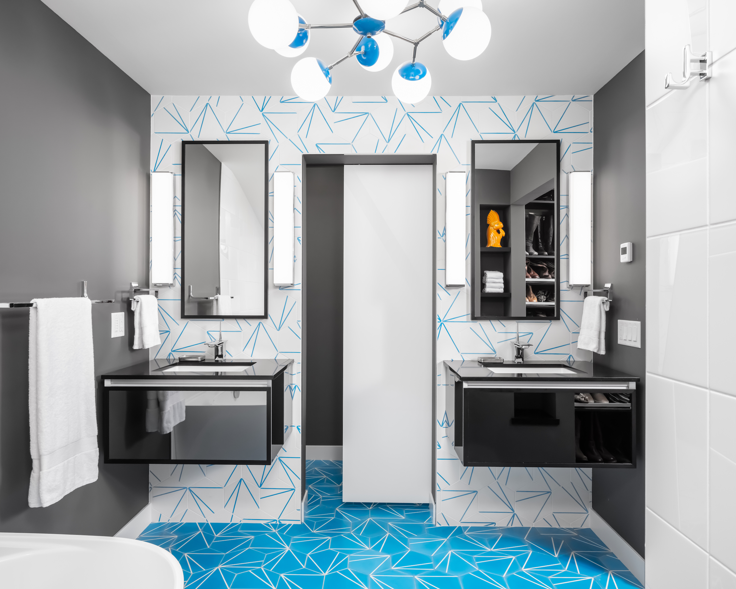 Mid-Century Moxie: A Master Bath Makeover. Modern bathroom remodel with cerulean blue floor tiles and geometric shower floor.  Features soaking tub, polished chrome fixtures, and retro atomic-age light fixtures.