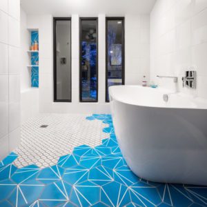 Mid-Century Moxie: A Master Bath Makeover. Modern bathroom remodel with cerulean blue floor tiles and geometric shower floor. Features polished chrome fixtures and double vanity.