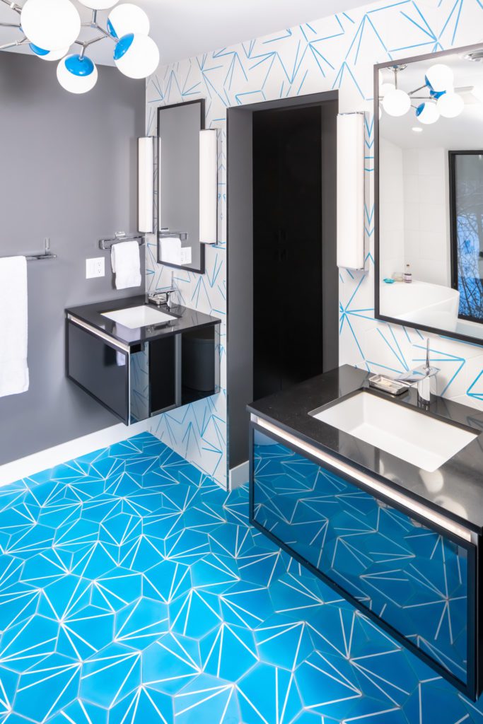 Mid-Century Moxie: A Master Bath Makeover. Modern bathroom remodel with cerulean blue floor tiles and geometric shower floor. Features polished chrome fixtures and double vanity.