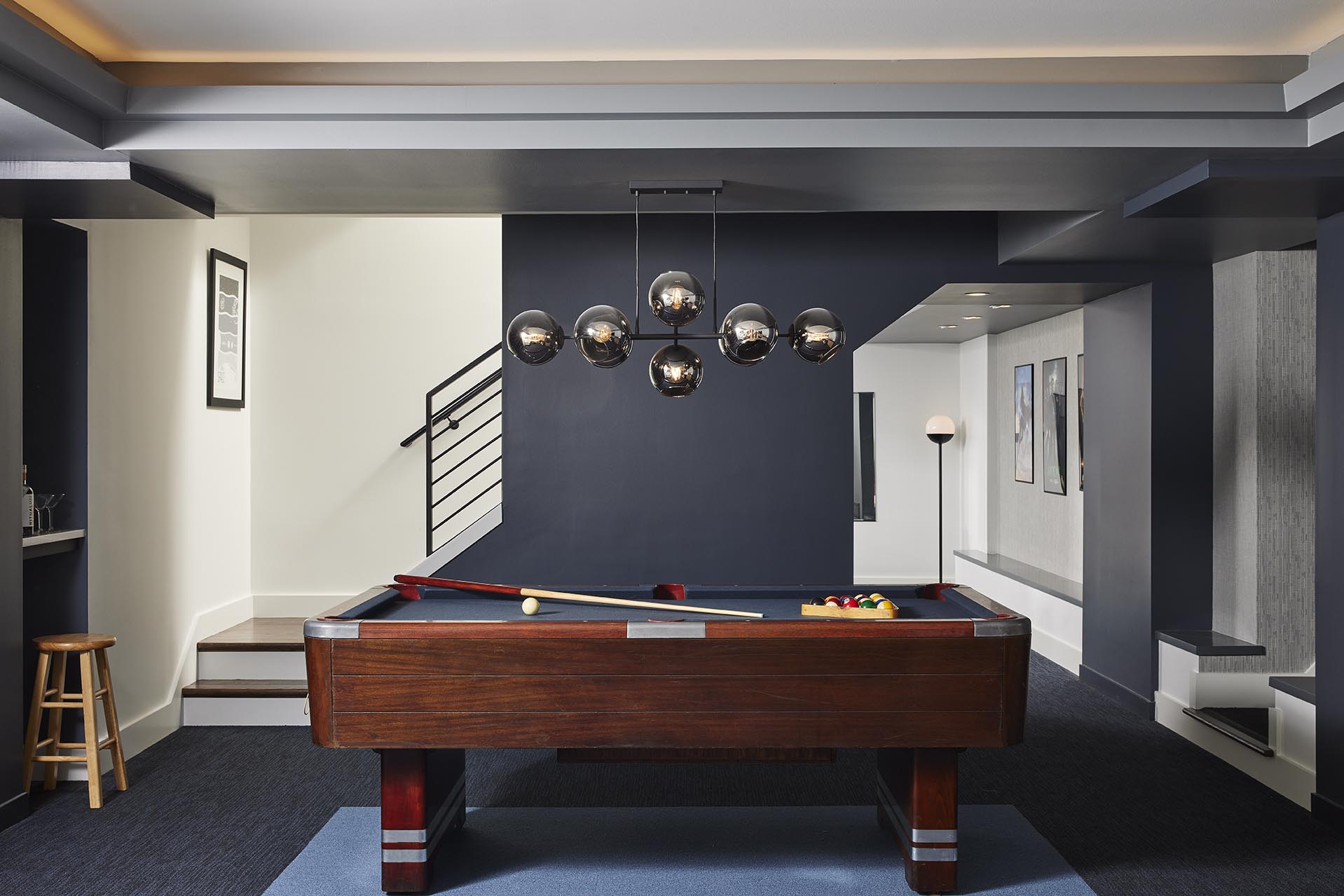 Pool table in the center of a finished basement with stairs in background and modern light fixture